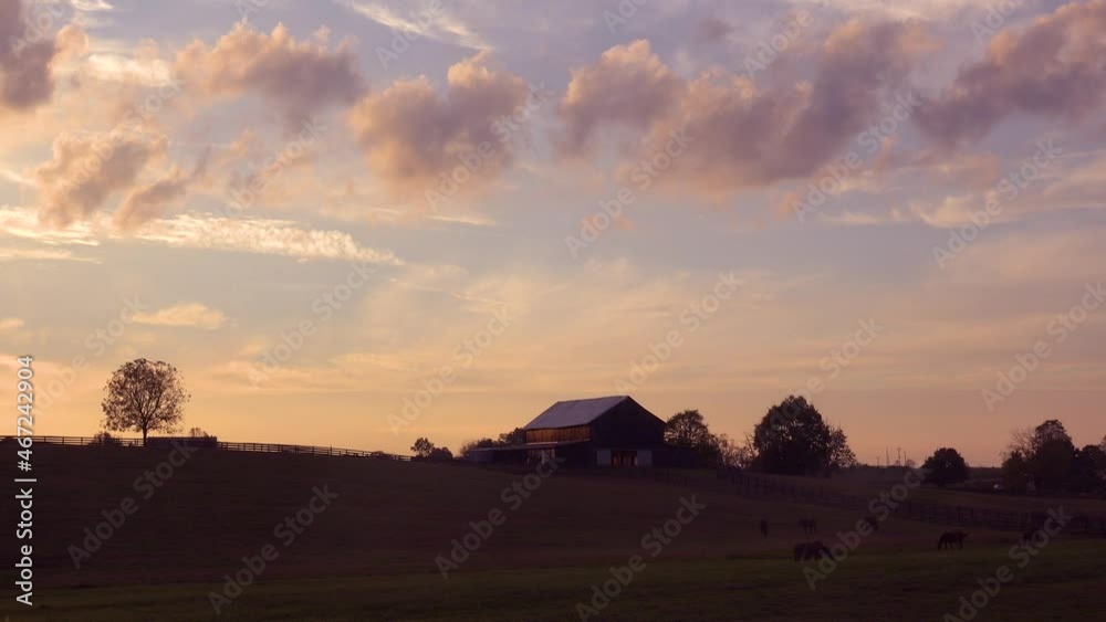 Clouds drift above a beautiful barn and horses grazing in rural Kentucky.