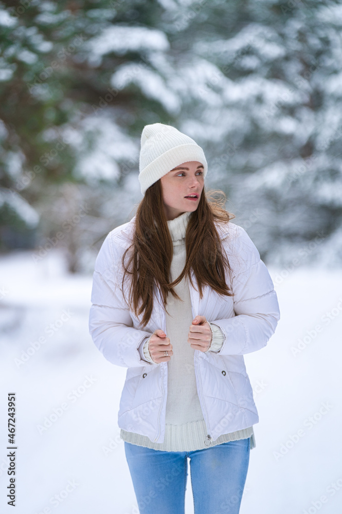 Fototapeta premium Close up portrait of happy girl in sweater and a knitted hat enjoying winter moments, having fun on a snowy morning on a blurred background of wood