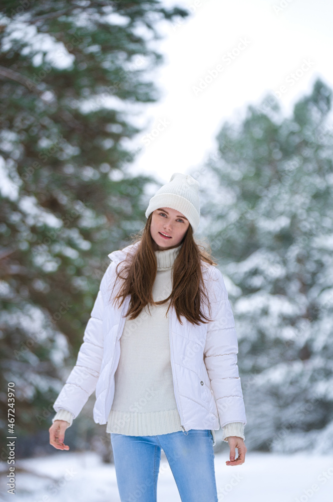 Fototapeta premium Close up portrait of happy girl in sweater and a knitted hat enjoying winter moments, having fun on a snowy morning on a blurred background of wood