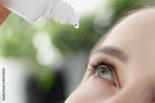 Woman dripping moisturizing drops into her eye closeup photo