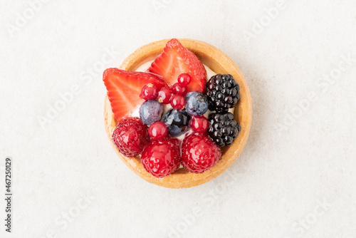 Freshly backed tartlet with strawberries, blueberries, raspberries on beige stone background. Top view, flat lay of food photography minimal concept