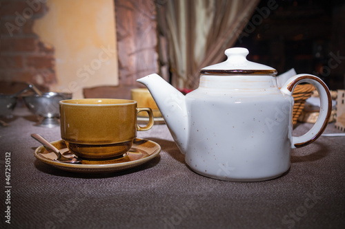 Brown cup and saucer and white ceramic teapot on table with gray tablecloth