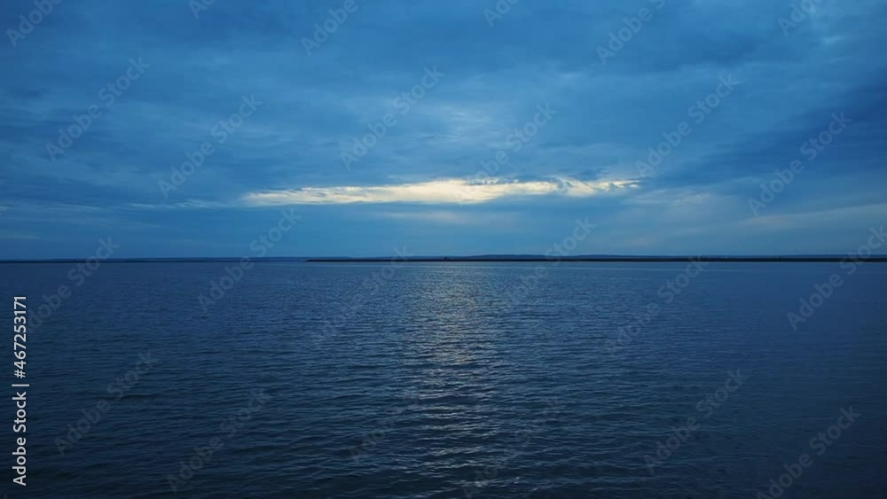 The color is blue. Silence over the water. A boat slowly ride on the water surface of a calm river, lake at sunset.
