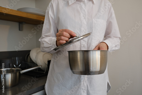 A woman holds a metal pan in her hands in the kitchen. Dishes close-up. Chef's working tools
