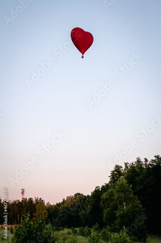 A hot air balloon flies over a green field. Composition of nature on a background of blue sky.
