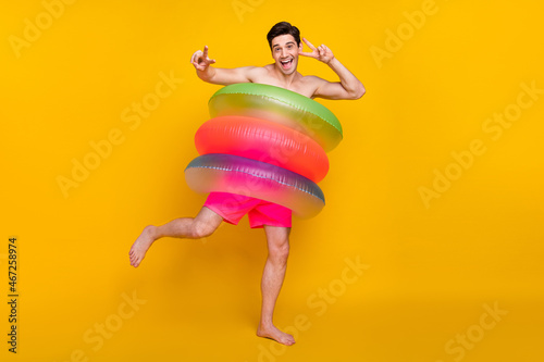 Full size photo of young man happy positive smile circle inflate bathing ocean show peace v-sign isolated over yellow color background