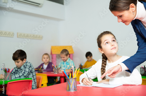 Friendly teacher woman helping girl during lesson in schoolroom. High quality photo