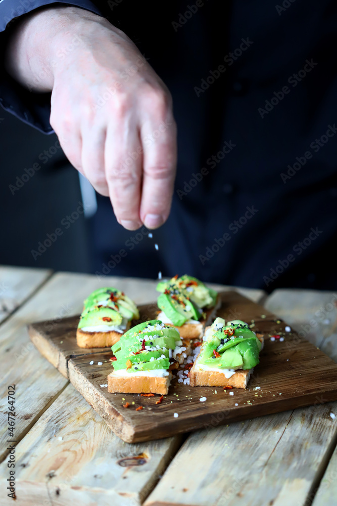 Chef prepares avocado toasts on a wooden board.