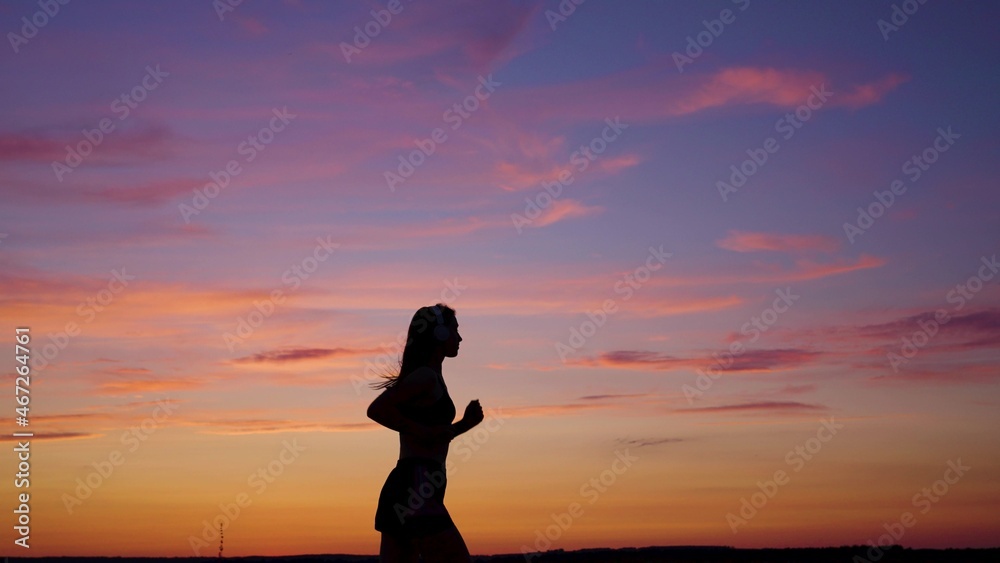 Silhouette of free young woman runs in summer in park at sunset, listens to music on headphones. Training jogging. Healthy jogging and outdoor exercise. Listen to music without Internet, play sports