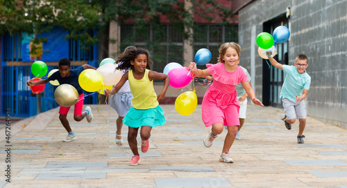 Group of happy kids running through streets with balloons in hands.