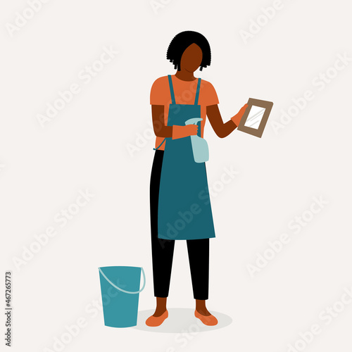 Black Female Cleaner With Apron Cleaning A Photo Frame. Cleaning Service Occupation.