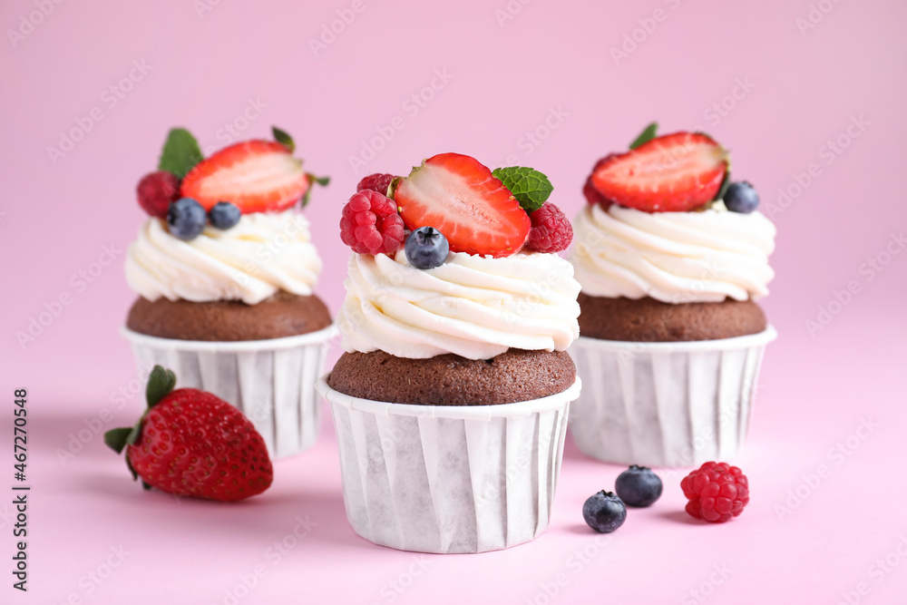 Delicious cupcakes with cream and berries on pink background