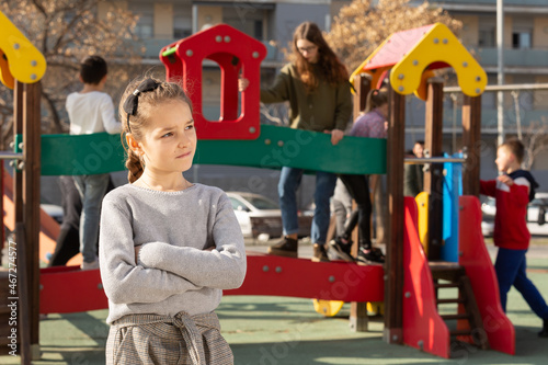 Portrait of offended girl not playing with friends after quarrel on playground. High quality photo