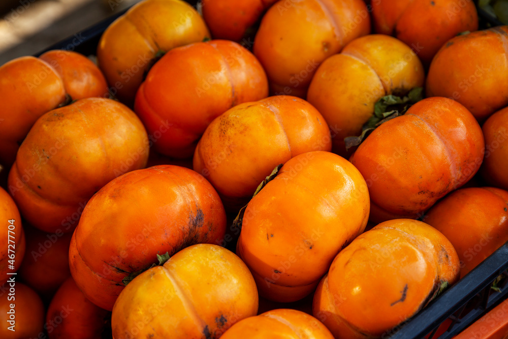 Ripe juicy persimmon in sunlight in a box on the market. Close-up. Vitamins and health from nature.