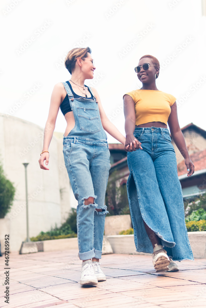 a couple of young women walk down the street holding hands during a sunny day. High quality photo