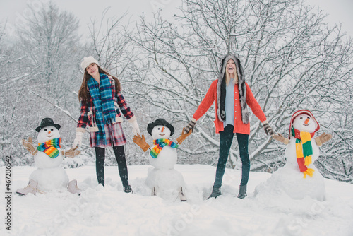 Group of girls with snowman outdoors. Students winter party and Christmas celebration. Two Joyful young women having fun with snowman. Merry Christmas and Happy new year.