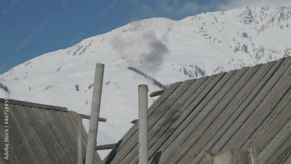 Smoke rising from chimney of rustic log cabins with a view of snowy mountain Smoke rising from chimney of rustic log cabins with a view of snowy mountain