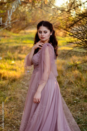 A young long-haired brown-haired woman in a long pink dress in a clearing