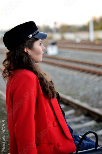 A young long-haired brown-haired woman in a black beret and a red coat on the station platform