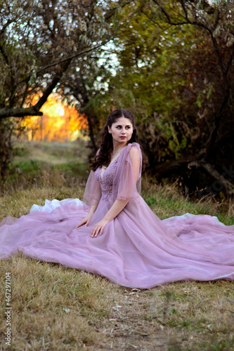 A young long-haired brown-haired woman in a long pink dress in a clearing