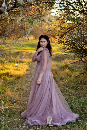 A young long-haired brown-haired woman in a long pink dress in a clearing