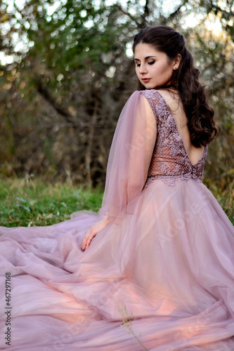 A young long-haired brown-haired woman in a long pink dress in a clearing