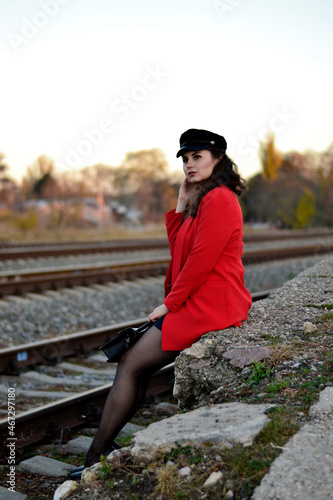 A young long-haired brown-haired woman in a black beret and a red coat on the station platform