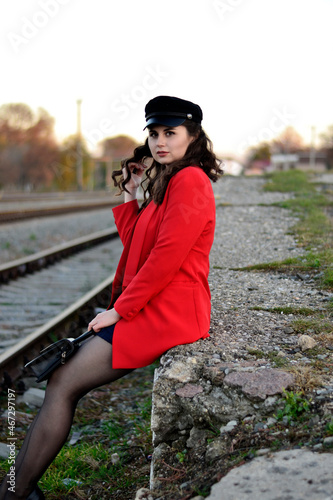 A young long-haired brown-haired woman in a black beret and a red coat on the station platform