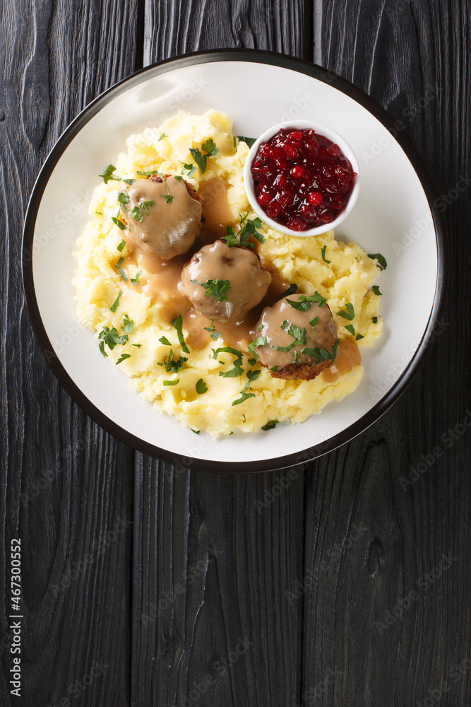 Finnish meatballs with gravy served with mashed potatoes and lingonberry jam close-up in a plate on the table. vertical top view above