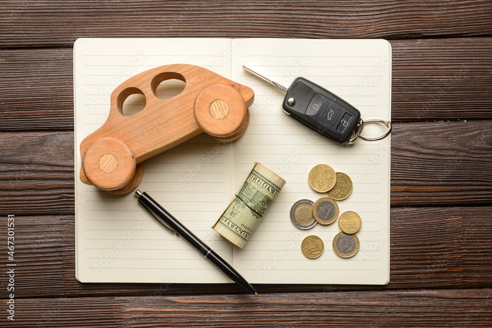 Wooden car with money, key and notebook on dark wooden background Wooden car with money, key and notebook on dark wooden background