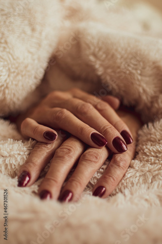 Female hands with dark red nails. Neat and elegant manicure for a lady. Royal bordeaux color on fingernails. Selective focus on the details, blurred background.