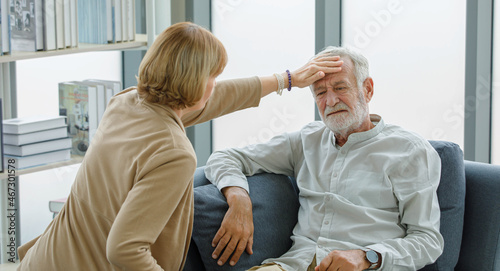 Caucasian old senior elderly supportive wife sitting use hand testing temperature from unhealthy gray bearded and hair husband forehead when he lying down on sofa get sick having cold and headache © Bangkok Click Studio
