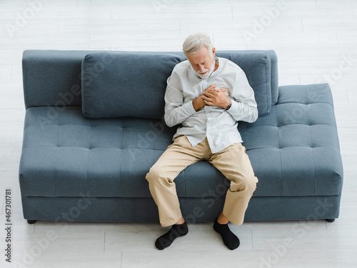 Caucasian old senior elderly gray hair and bearded man lying down close eyes on sofa in living room at home alone holding hands on chest suffering from sudden problem painful emergency heart attack © Bangkok Click Studio