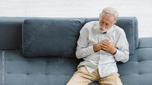 Caucasian old senior elderly gray hair and bearded man lying down close eyes on sofa in living room at home alone holding hands on chest suffering from sudden problem painful emergency heart attack © Bangkok Click Studio
