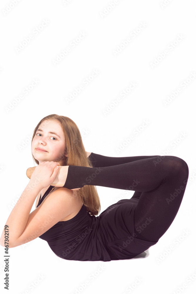 Sport Ideas and Concepts. Optimistic Caucasian Sportswoman Rhythmic Gymnast In Training Black Outfit Posing Indoors During Backward Legs Twist Stretching Exercises On White. Sport Ideas and Concepts. Optimistic Caucasian Sportswoman Rhythmic Gymnast In Training Black Outfit Posing Indoors During Backward Legs Twist Stretching Exercises On White.