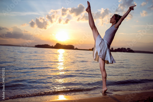 Passion and Love for Dance With Japanese Ballet Dancer in White Dress And Silver Crown Standing In Ocean Waves And Showing Ballet Pas With Lifted Hands Against Picturesque Sunset At Sea. © danmorgan12