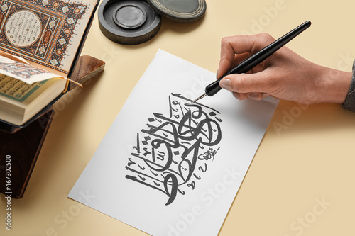 Arabic calligraphist writing on paper sheet against color background photo