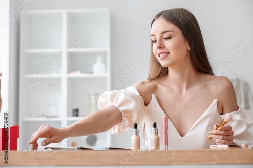 Pretty young woman with makeup brush sitting at table in dressing room