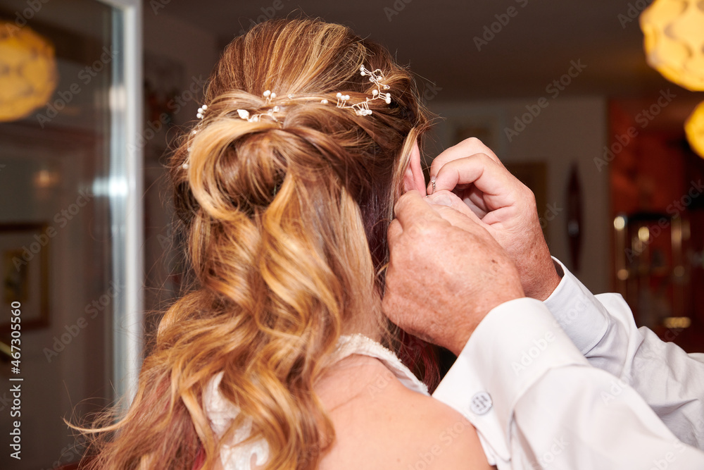 Fototapeta premium Closeup shot of male hands putting an earring on the bride's ear
