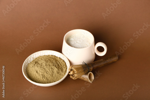 Bowl with hojicha powder, cup of tea and chasen on brown background photo