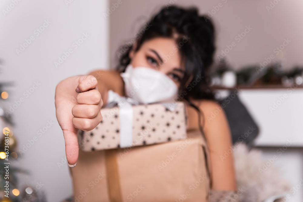 Upset sad woman opening wrapped ribbon gift box present,wear blue face disposable mask New Year evening, Christmas decorated tree. Hand gesture thumb down dislike lockdown holiday Upset sad woman opening wrapped ribbon gift box present,wear blue face disposable mask New Year evening, Christmas decorated tree. Hand gesture thumb down dislike lockdown holiday