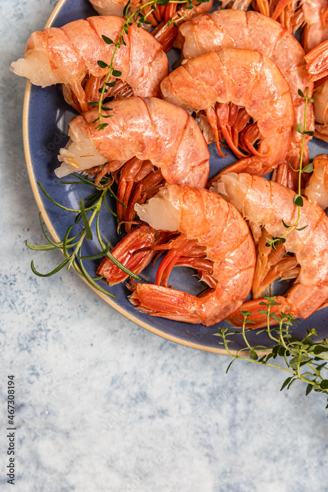 Raw red Argentine shrimps on ceramic plate, blue concrete background. Ocean jumbo shrimps. Top view.