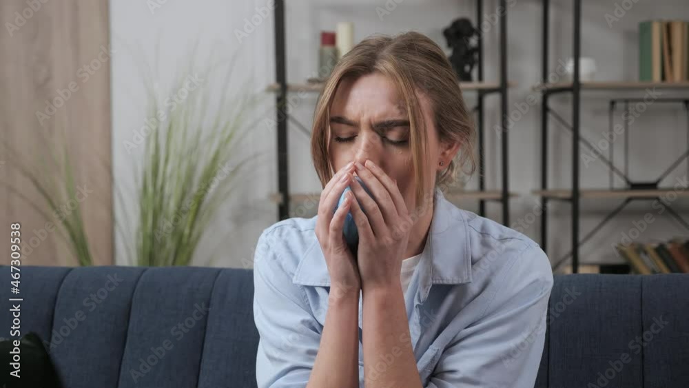 Beautiful blonde girl dressed in casual clothes coughs during covid pandemic 19 at home. Inflammation of the respiratory tract, virus, infection. Woman coughs into a medical mask and feels bad indoor. Beautiful blonde girl dressed in casual clothes coughs during covid pandemic 19 at home. Inflammation of the respiratory tract, virus, infection. Woman coughs into a medical mask and feels bad indoor.