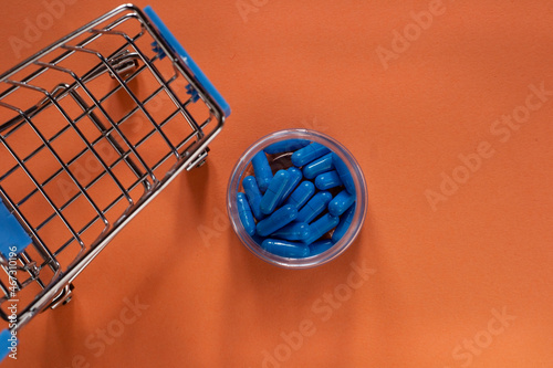 Wallpaper Mural Blue capsules next to a small supermarket trolley. Delivery of pills from pharmacies. Blue capsules on an orange background.  Torontodigital.ca