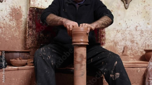 adult man in work clothes makes a pot on a potter's wheel