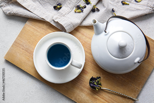 Teapot and cup of organic blue tea on light background