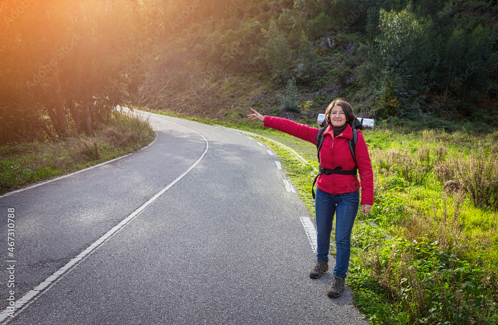 A woman tourist, in a jacket, hitchhiking on the road, walks along the Portuguese forest roads. Stops fellow travelers. Sunny day. A woman tourist, in a jacket, hitchhiking on the road, walks along the Portuguese forest roads. Stops fellow travelers. Sunny day.