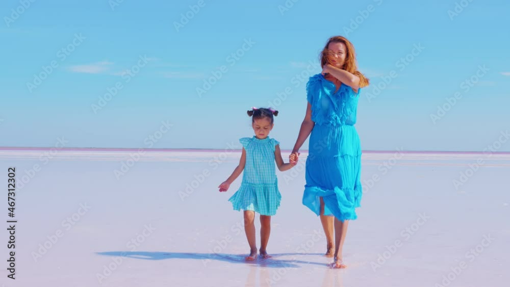 Mother and daughter walk along salt lake holding hands in sunny day. Young woman with girl spend time at health resort. Family vacation in unique natural location. Treatment, rest, recreation Mother and daughter walk along salt lake holding hands in sunny day. Young woman with girl spend time at health resort. Family vacation in unique natural location. Treatment, rest, recreation