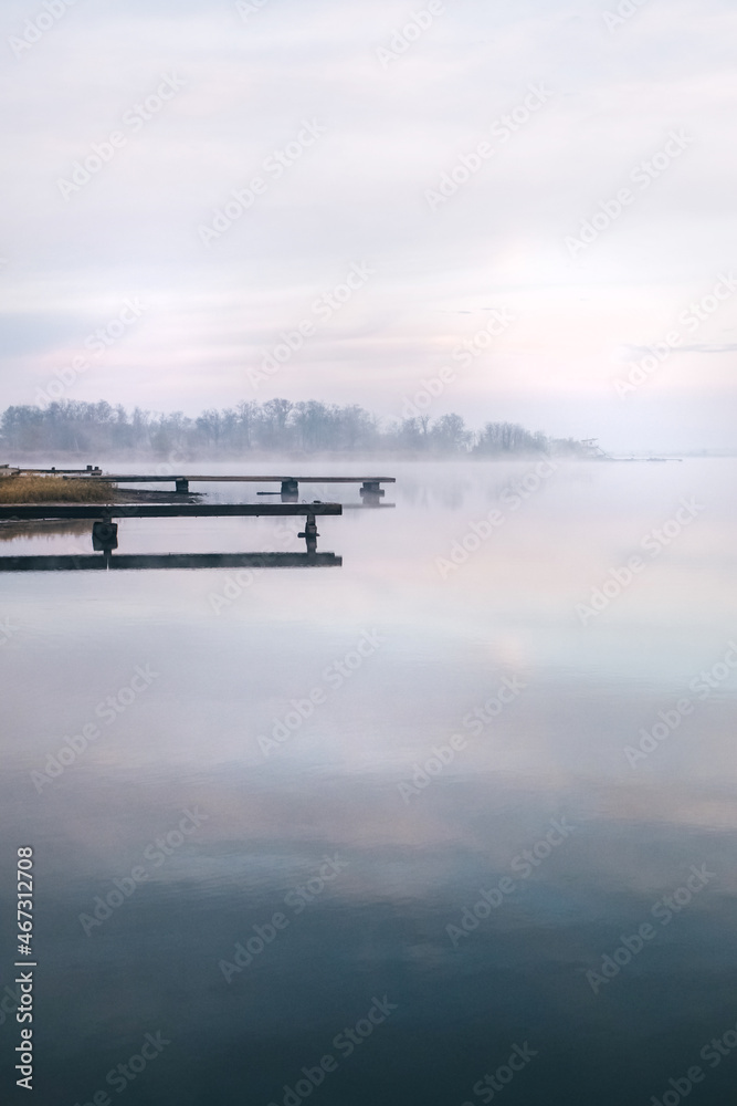 General plan of the pier for fishermen, which is located on a misty lake. The mist on the water creates the feeling of a magical effect. Clouds bounce off the surface. Place for text