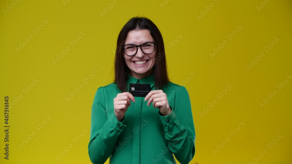 brunette shows her bank card that she is the best, she is washed short, wears glasses, wears a green shirt, the background is yellow brunette shows her bank card that she is the best, she is washed short, wears glasses, wears a green shirt, the background is yellow
